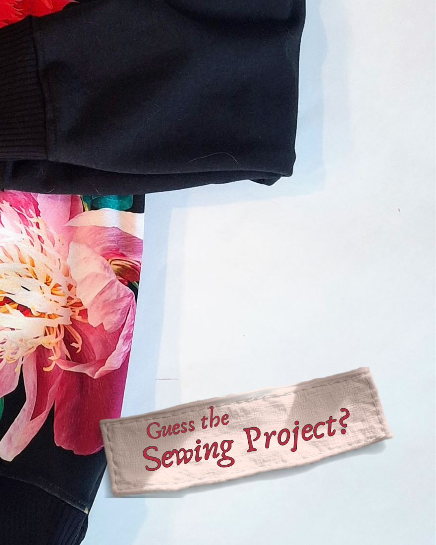 A folded black garment with a colorful floral print partially visible underneath, placed on a light blue background next to a beige fabric tag that reads 'Guess the Sewing Project?'.